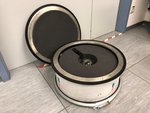 Auf einem grauen Fußboden steht eine metallische Box. Der Deckel ist offen und steht daneben. Im Inneren ist eine kleine Kugel in Verpackungsmaterial eingebettet.