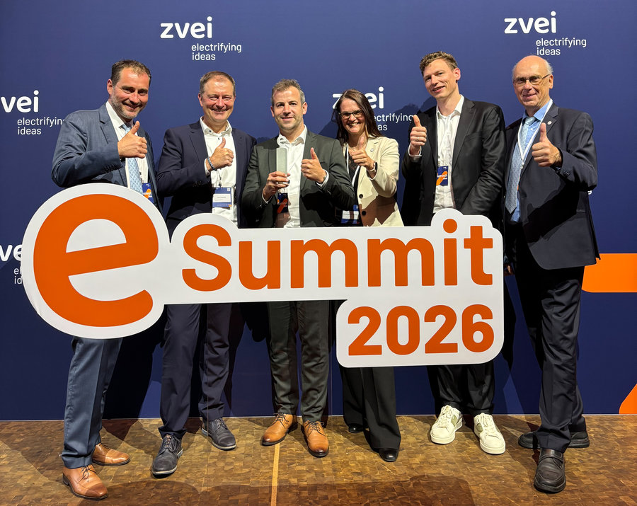 Gewinnerteam Eine Gruppe Menschen steht hinter einer großen Schrifttafel mit der Aufschrift "eSummit 2026"