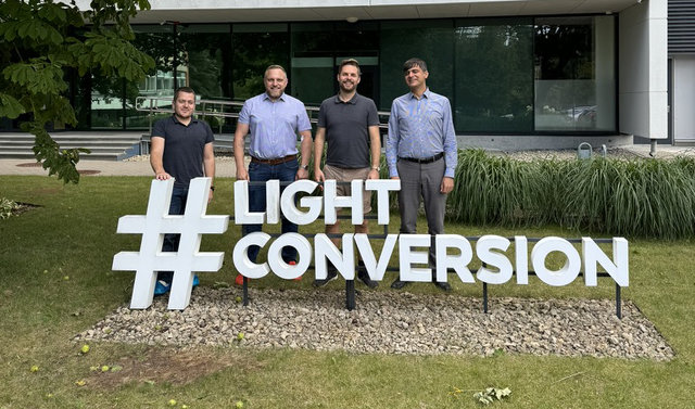 Vier Männer stehen auf einer grünen Wiese vor einem Gebäude und hinter der Aufschrift "Light Conversion".